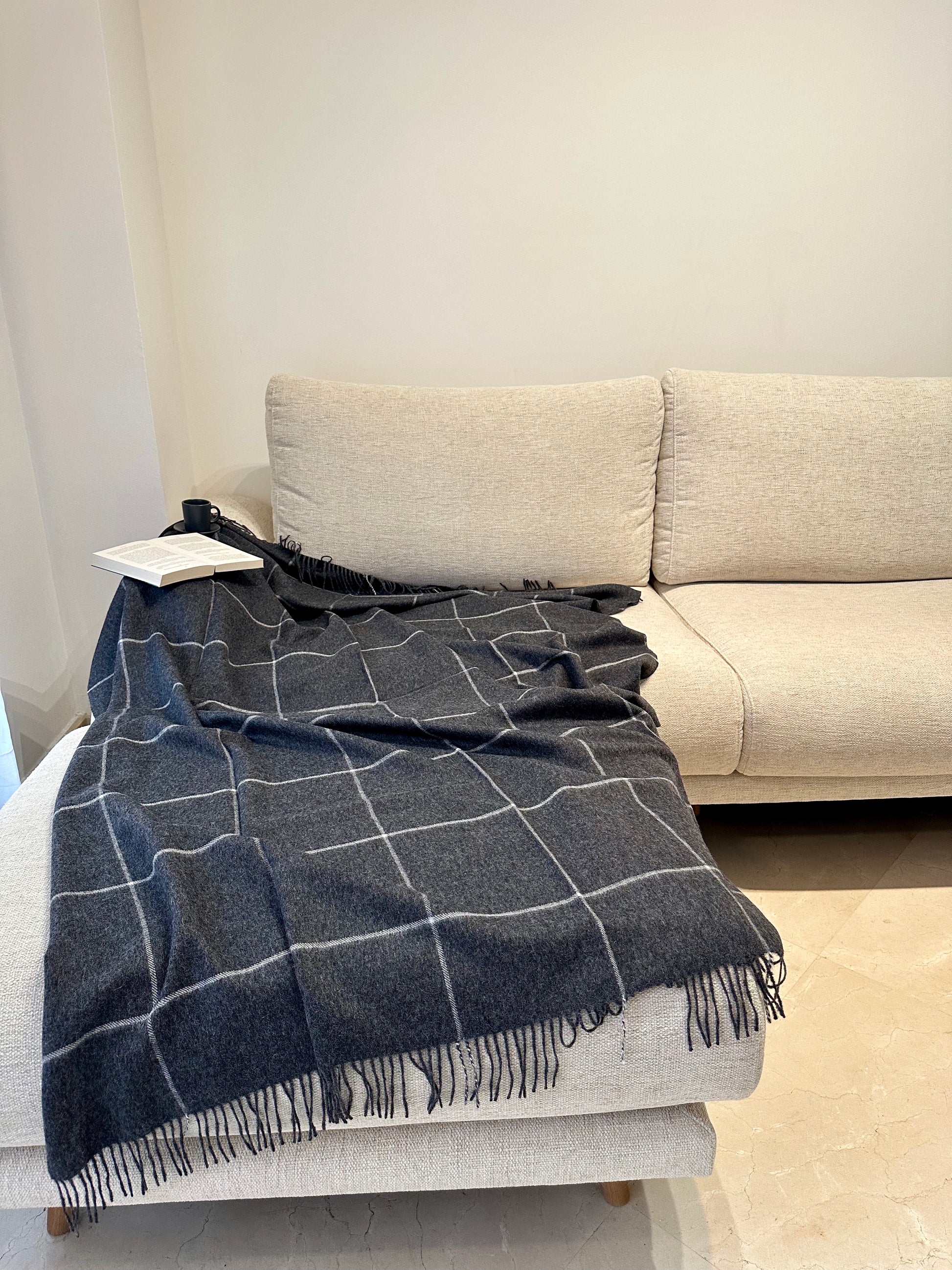 Elegant grey alpaca plaid blanket neatly folded on a sofa, a luxurious and cozy throw adding warmth and comfort to your home.