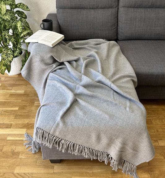 Elegant grey alpaca knit blanket draped over a bed, ideal for warmth and style.
